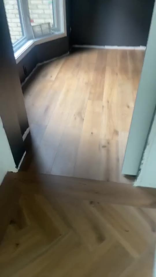 First frame of a real walkthrough video: a room with a new floor and no baseboards yet.